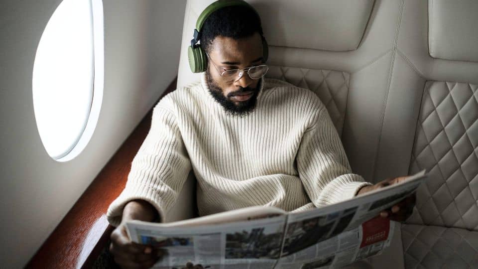 homem usando headphones bluetooth e lendo jornal no avião