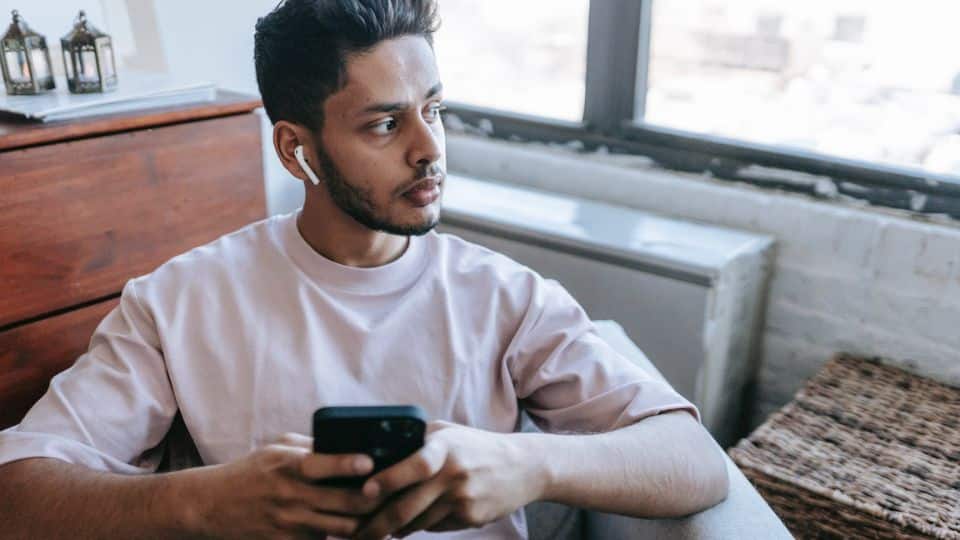 homem ouvindo música no fone bluetooth e mexendo no seu celular