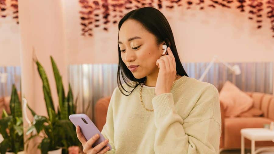 mulher manuseando fone de ouvido bluetooth enquanto olha para o celular