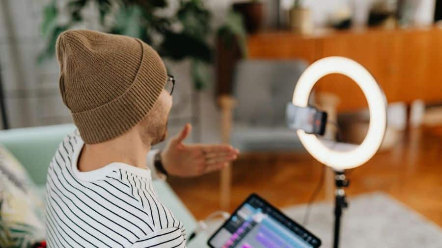 Criador de conteúdo gravando vídeo com um ring light, utilizando tablet e smartphone em um ambiente doméstico