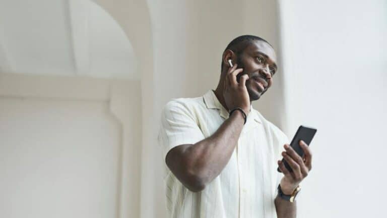 Homem sorrindo enquanto utiliza AirPods e segura um smartphone, simbolizando conectividade e praticidade