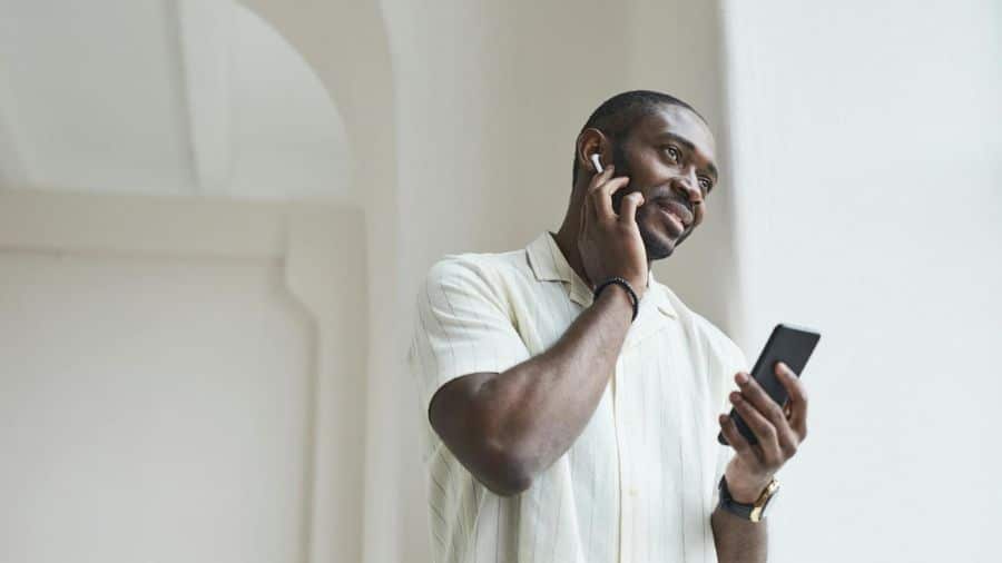 Homem sorrindo enquanto utiliza AirPods e segura um smartphone, simbolizando conectividade e praticidade