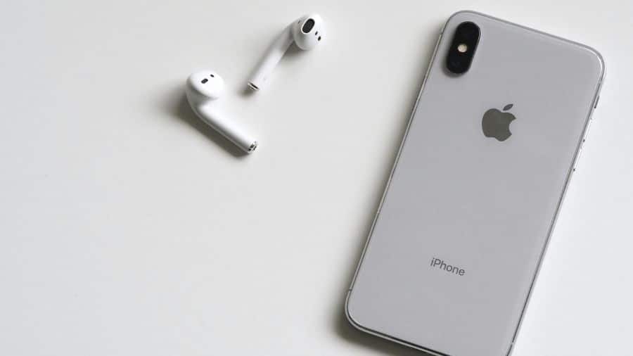 AirPods ao lado de um iPhone sobre uma superfície branca, destacando o design característico dos dispositivos da Apple