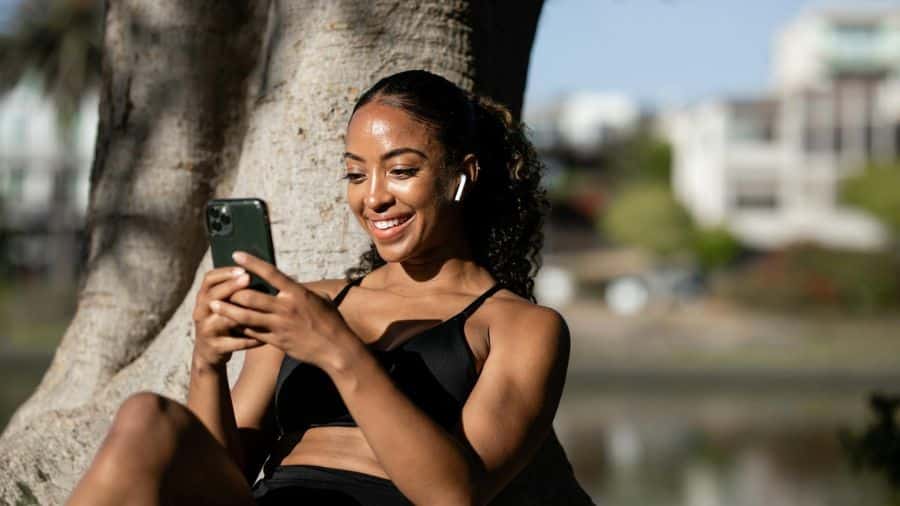 Mulher ao ar livre usando fones de ouvido e smartphone, simbolizando proteção IPX4 contra respingos em atividades externas