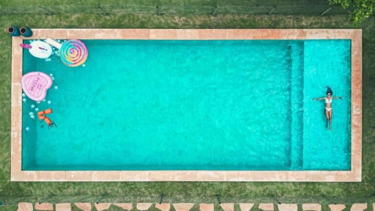 Vista aérea de uma piscina com objetos flutuantes e uma pessoa nadando, representando resistência à água, conceito do grau de proteção IPX4