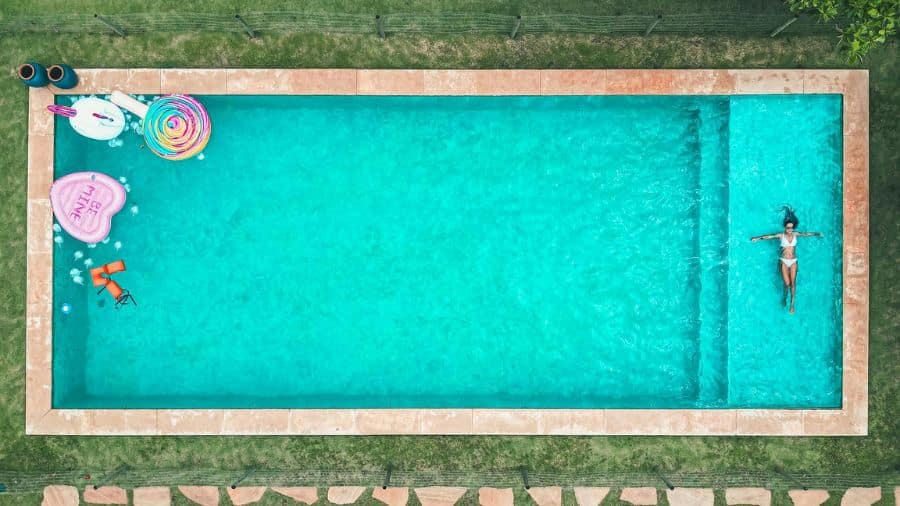 Vista aérea de uma piscina com objetos flutuantes e uma pessoa nadando, representando resistência à água, conceito do grau de proteção IPX4